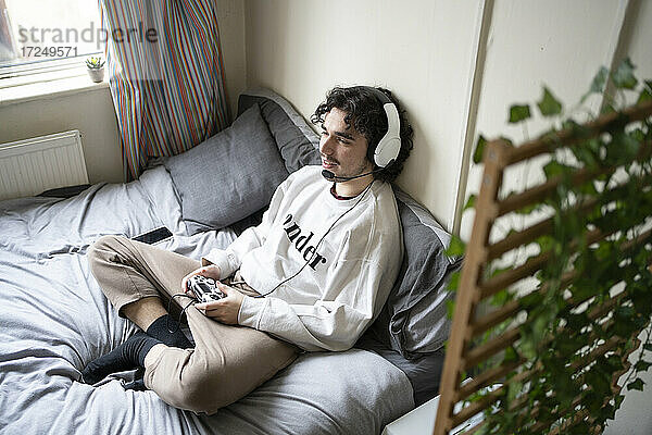 Junger Mann mit Kopfhörern spielt ein Videospiel zu Hause