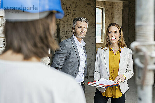 Weiblicher Kollege im Gespräch mit einem Bauarbeiter  während er neben einem männlichen Architekten steht