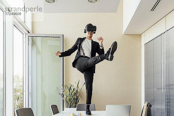 Junge Unternehmerin mit Virtual-Reality-Headset  die auf dem Schreibtisch im Büro steht und kickt