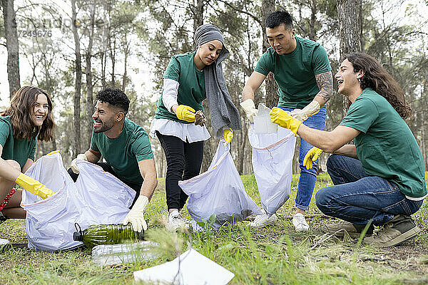 Lächelnde männliche und weibliche Freiwillige sammeln Plastik im Wald