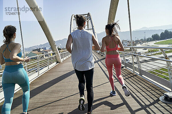 Männliche und weibliche Freunde joggen auf einer Brücke an einem sonnigen Tag