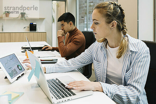 Geschäftsfrau verwendet digitales Tablet  während sie neben einem Kollegen im Büro sitzt