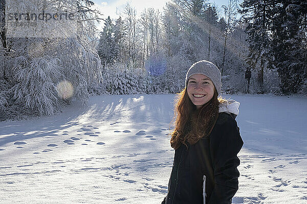 Lächelnde schöne Frau im Schnee stehend an einem sonnigen Tag