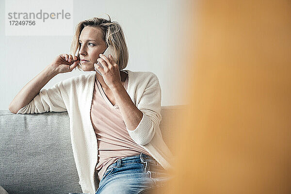 Frau schaut weg  während sie zu Hause mit dem Handy telefoniert