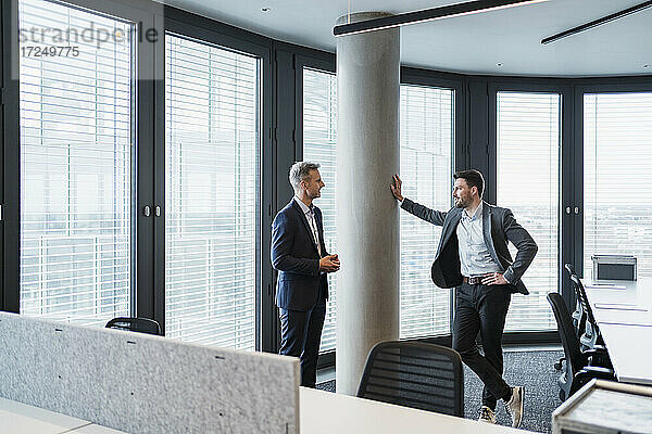 Geschäftsleute im Gespräch  während sie an einer architektonischen Säule im Büro stehen