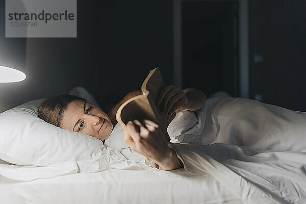 Frau liest ein Buch  während sie auf dem Bett im Hotelzimmer liegt
