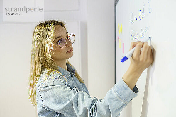 Blonde Geschäftsfrau  die in einer Besprechung im Büro auf ein Whiteboard schreibt