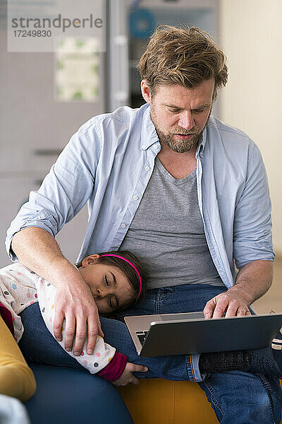 Geschäftsmann  der sich um ein Mädchen kümmert  während er zu Hause einen Laptop benutzt