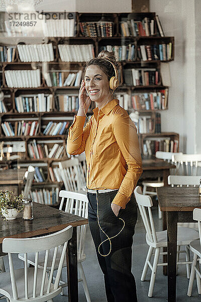 Unternehmerin mit Hand in der Tasche hört Musik über Kopfhörer in einem Cafe