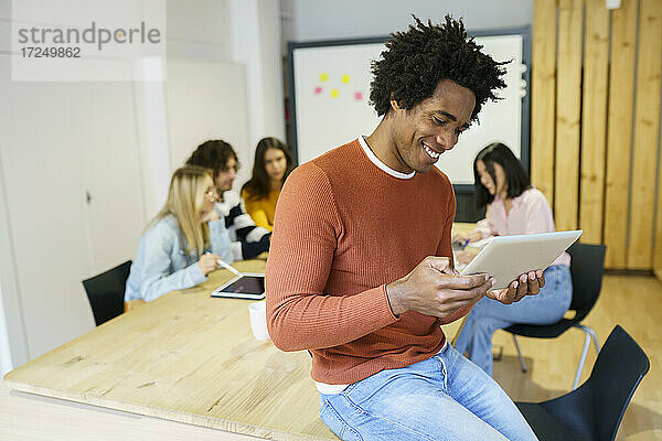 Lächelnder männlicher Geschäftsmann  der ein digitales Tablet am Bürotisch benutzt