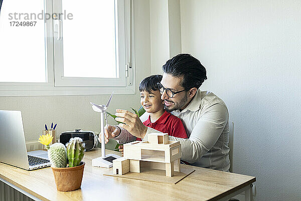 Männlicher Architekt erklärt seinem Sohn zu Hause das Modell einer Windkraftanlage