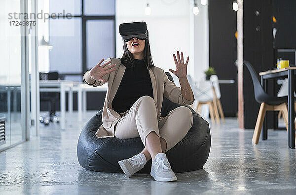 Weibliche Fachkraft gestikuliert  während sie auf einem Sitzsack in einem Coworking-Büro virtuelle Realität genießt