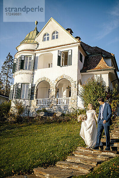 Ein frisch verheiratetes Paar geht die Treppe vor einer Villa hinunter