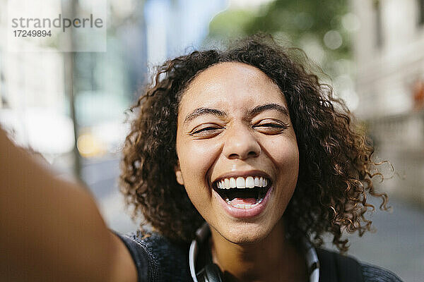 Lachende junge Frau nimmt Selfie in der Stadt