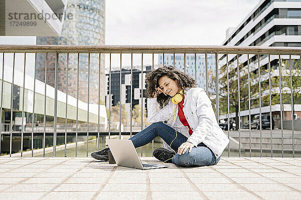 Junge Frau  die auf dem Gehweg sitzend einen Laptop benutzt