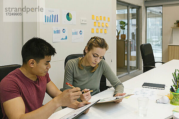Männliche und weibliche Fachkräfte arbeiten an Finanzberichten am Schreibtisch in einem Coworking-Büro