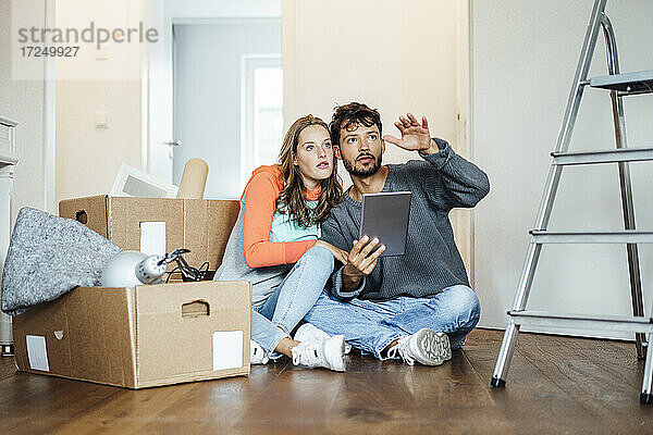 Junges Paar sitzt mit digitalem Tablet und diskutiert im neuen Haus