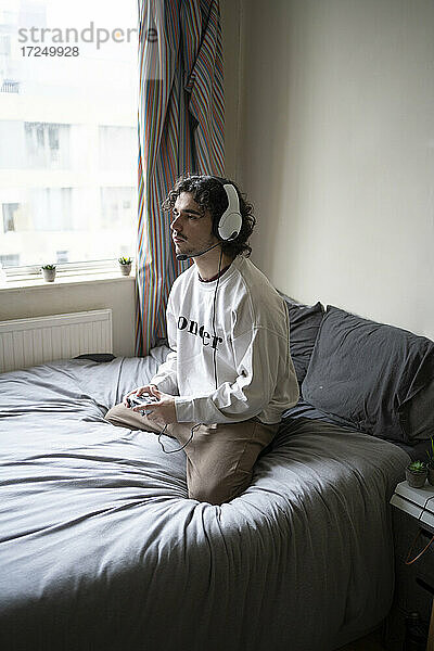 Mann kniend beim Spielen eines Videospiels auf dem Bett zu Hause
