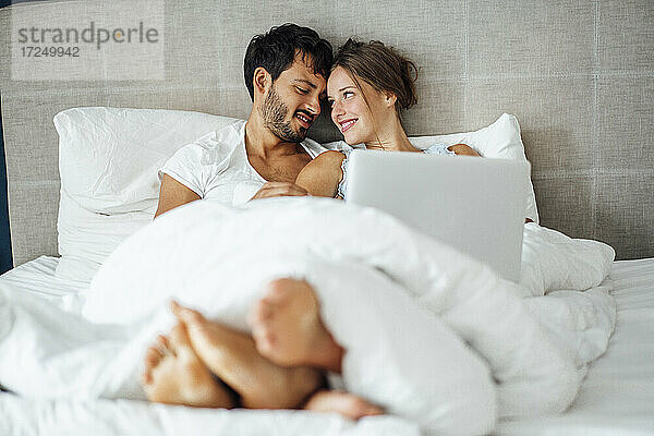 Lächelndes Paar  das sich auf dem Bett sitzend gegenseitig ansieht