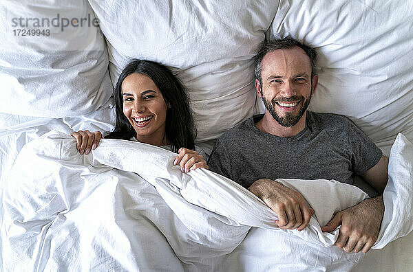 Glückliches Paar mit Decke auf dem Bett liegend zu Hause