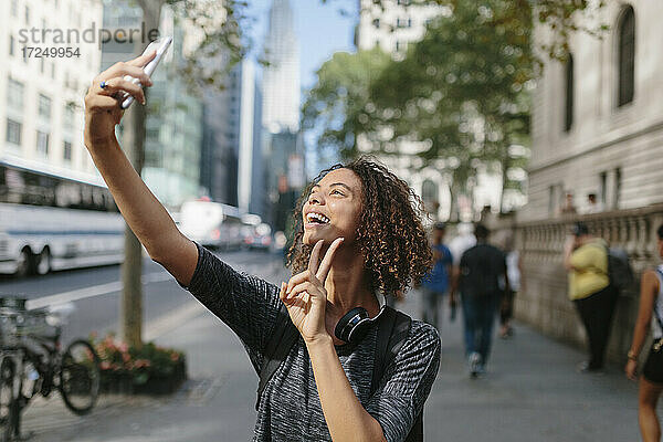 Frau zeigt Friedenszeichen  während sie ein Selfie mit dem Handy in der Stadt macht