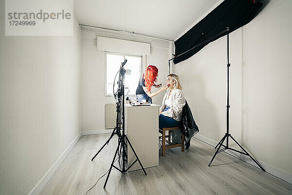 Make-up-Künstlerin trägt Gesichtspuder auf ein Modell auf  während sie im Studio bloggt