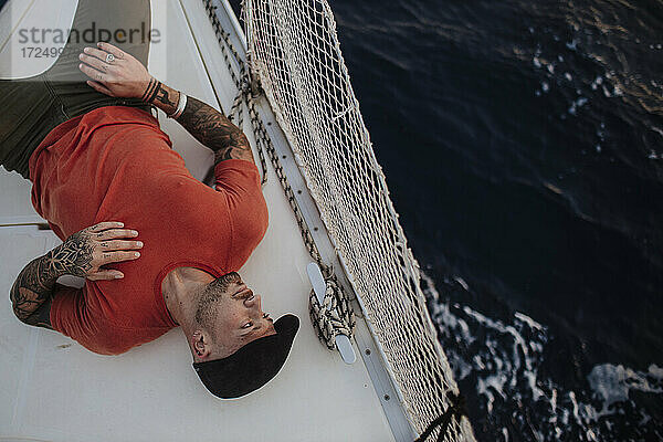 Hipster-Mann schaut weg  während er auf einem Boot im Meer liegt