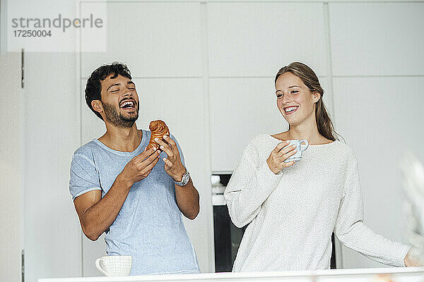 Glücklicher Mann mit Croissant bei seiner Freundin in der Küche zu Hause