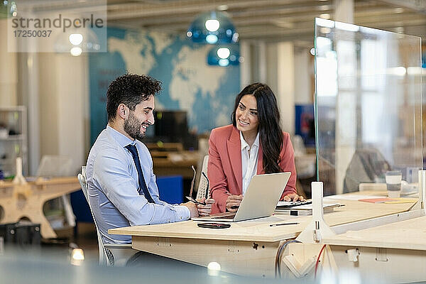 Lächelnde Geschäftsfrau  die einen männlichen Kollegen ansieht  während sie einen Geschäftsplan im Büro bespricht