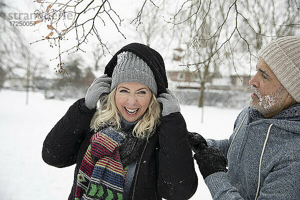 Lachende Frau mit Kapuze  die von einem Mann im Winter getragen wird