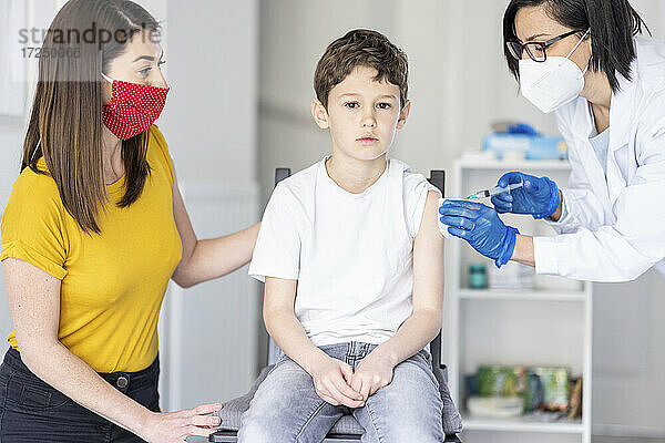 Mutter betrachtet ihren Sohn  der von einer Ärztin in einer Klinik während der Pandemie gegen COVID geimpft wird
