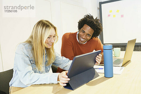 Lächelnde multiethnische männliche und weibliche Fachkräfte arbeiten an einem digitalen Tablet im Büro