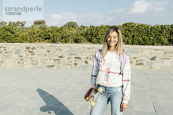 Lächelnde Frau mit Skateboard im Park an einem sonnigen Tag