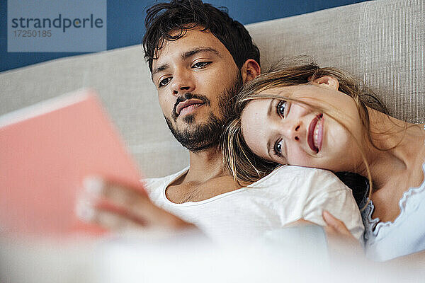 Junger Mann mit lächelnder Frau  die im Schlafzimmer ein Buch liest