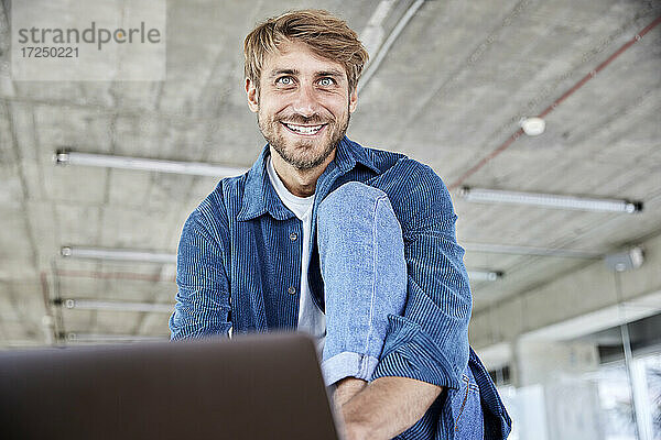 Lächelnder Mann mit Laptop auf dem Dachboden