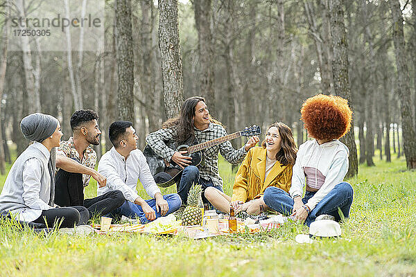 Junge männliche und weibliche Freunde spielen Gitarre beim Picknick im Wald