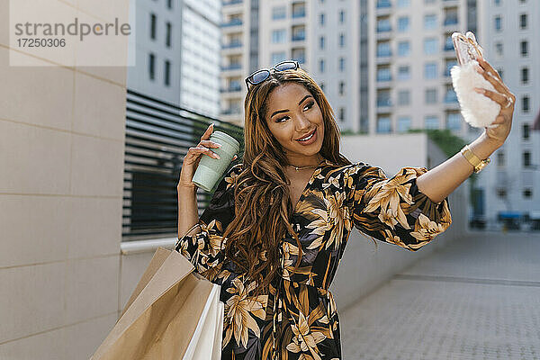 Schöne Frau  die eine Kaffeetasse hält und ein Selfie mit ihrem Smartphone auf einem Fußweg macht
