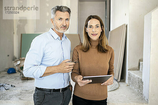 Weiblicher Kollege mit digitalem Tablet neben einem gut aussehenden männlichen Architekten auf der Baustelle