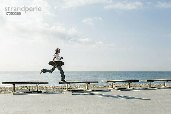 Frau mit Skateboard überquert Bank beim Laufen am Strand