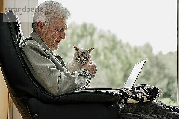 Älterer Mann mit Laptop und Katze im Wohnzimmer