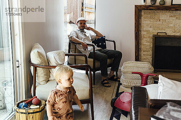 Vater betrachtet seinen kleinen Sohn  während er zu Hause auf einem Stuhl sitzt