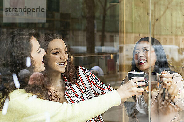 Fröhliche Freundinnen stoßen mit einem Getränk im Café an