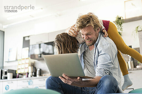 Wütender Geschäftsmann  der ein Mädchen auf der Schulter trägt  während er einen Laptop zu Hause hält