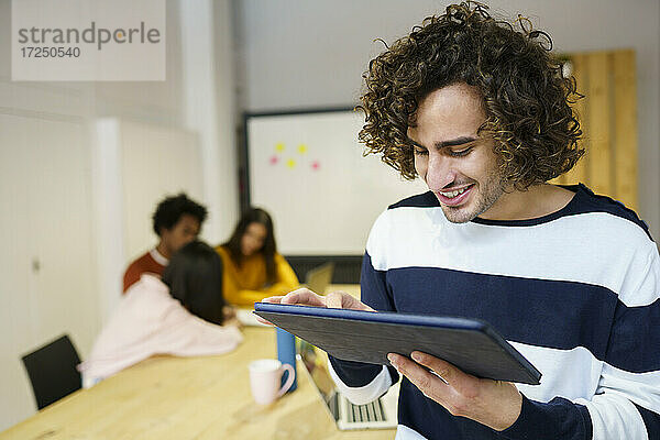 Lächelnder kreativer Geschäftsmann mit digitalem Tablet im Büro