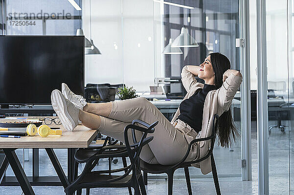 Geschäftsfrau mit Händen hinter dem Kopf entspannt am heißen Schreibtisch im Büro