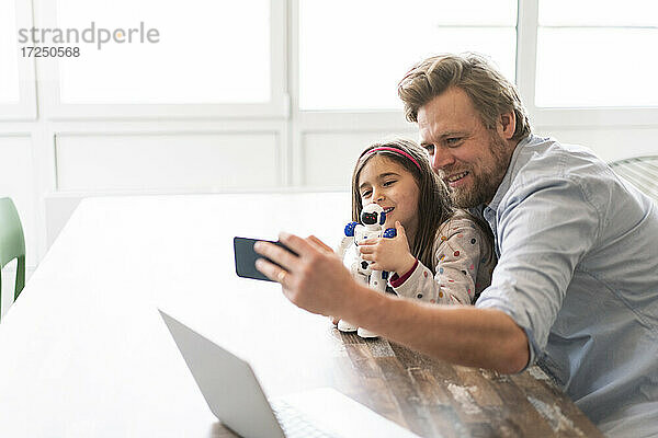 Vater  der ein Selfie mit seiner Tochter macht  die einen Spielzeugroboter über ein Mobiltelefon zu Hause hält