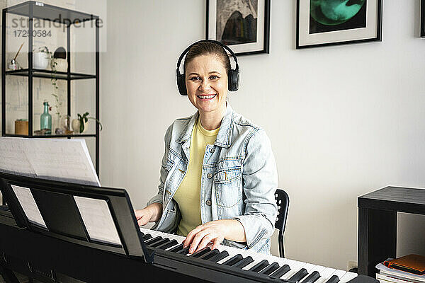 Lächelnde Pianistin mit Kopfhörern beim Klavierspielen zu Hause