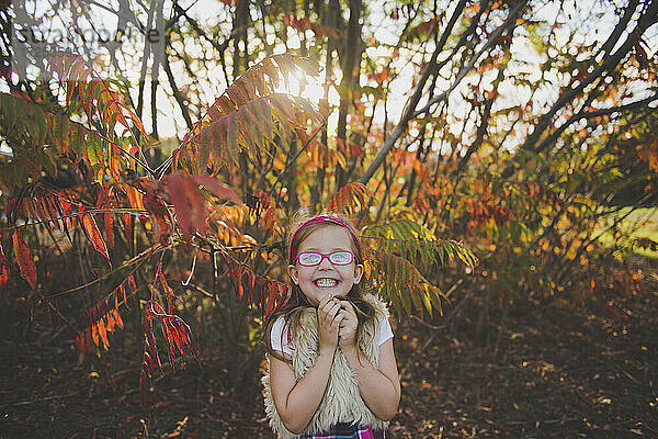 Lächelndes Mädchen mit Brille vor Pflanzen im Herbst