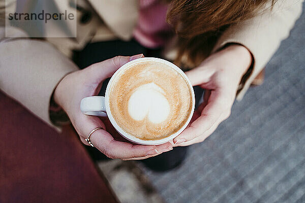Frau hält Cappuccinotasse in einem Straßencafé