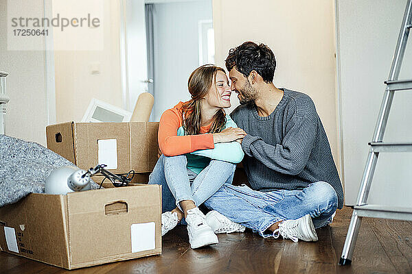 Lächelndes junges Paar sitzt zusammen bei einem Karton zu Hause